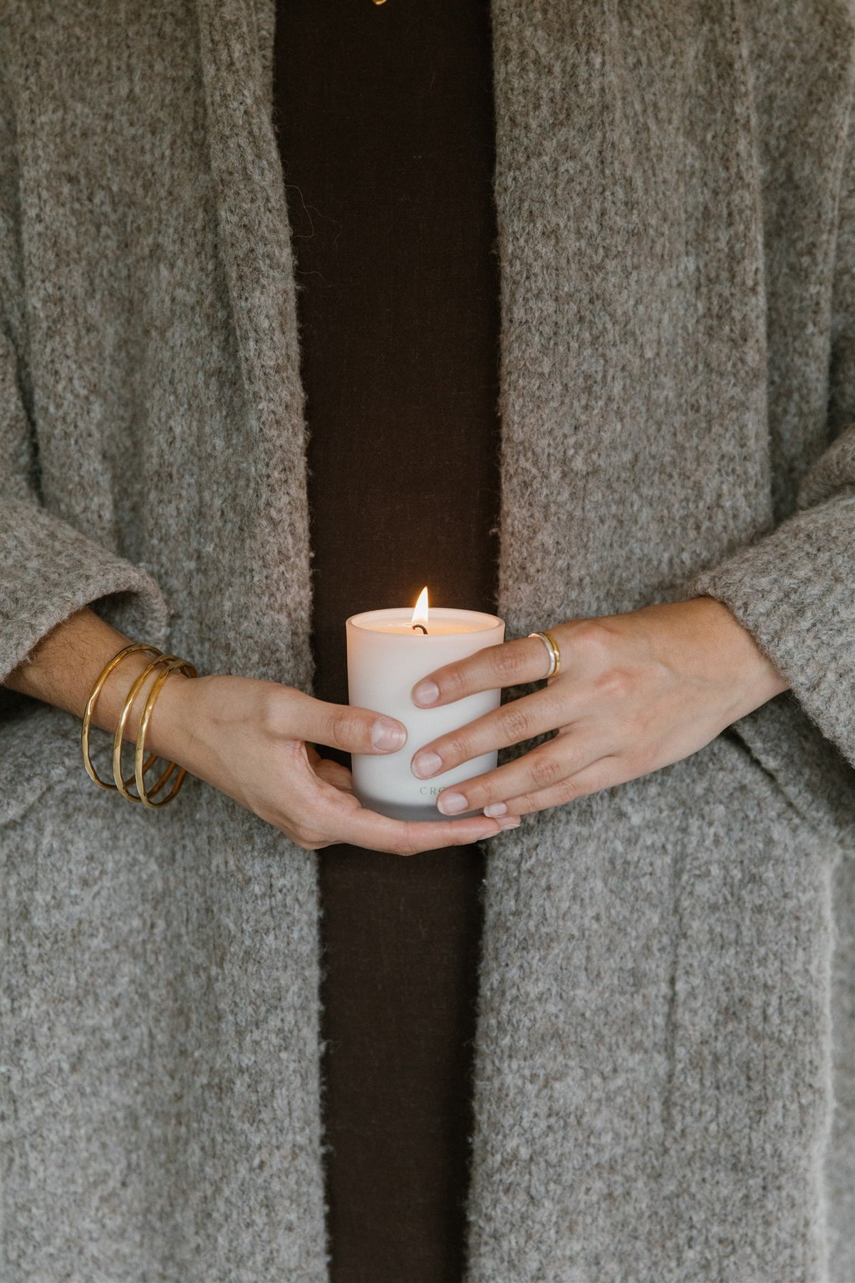 Hands holding a lit 11:11 Classic candle in a white glass jar against a grey wool cardigan
