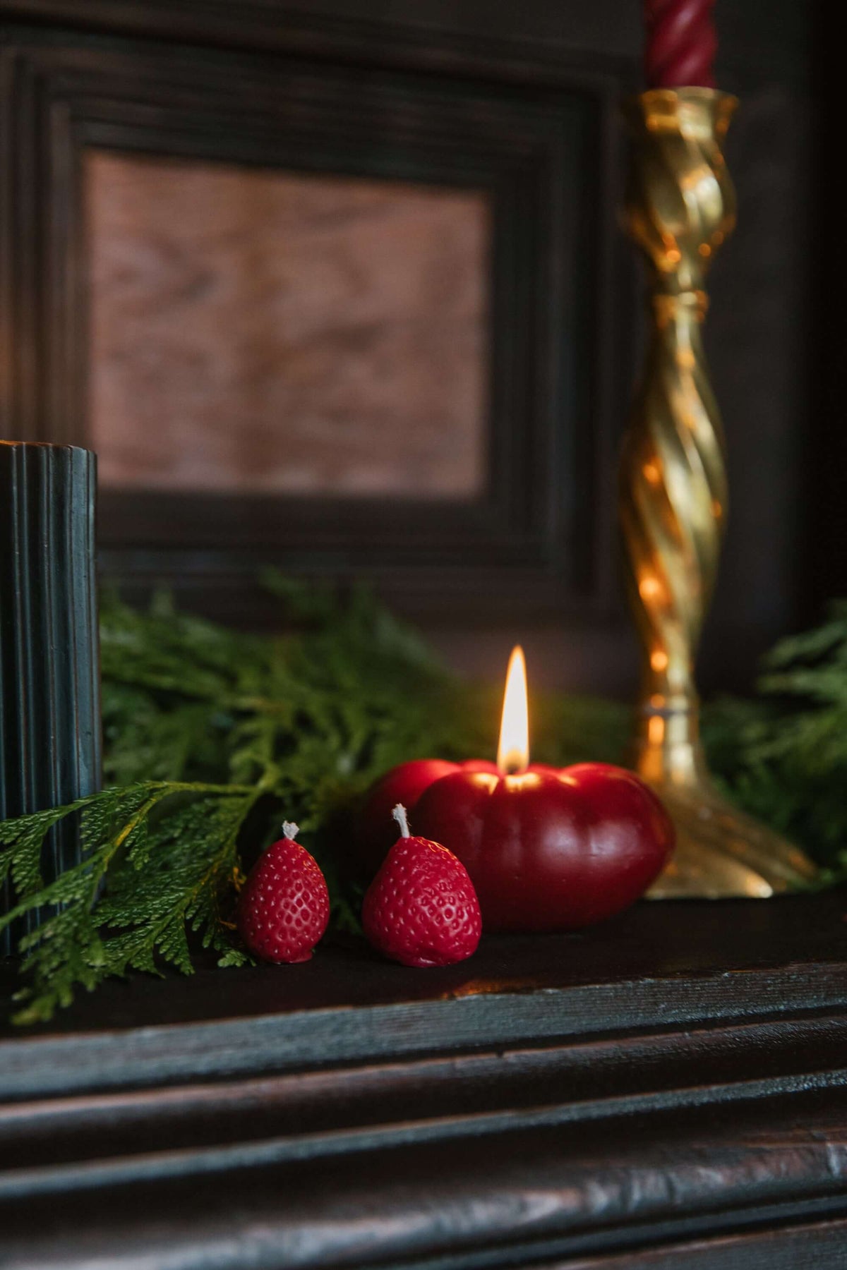 Heirloom tomato candle in a cozy setting with red strawberries and green foliage.
