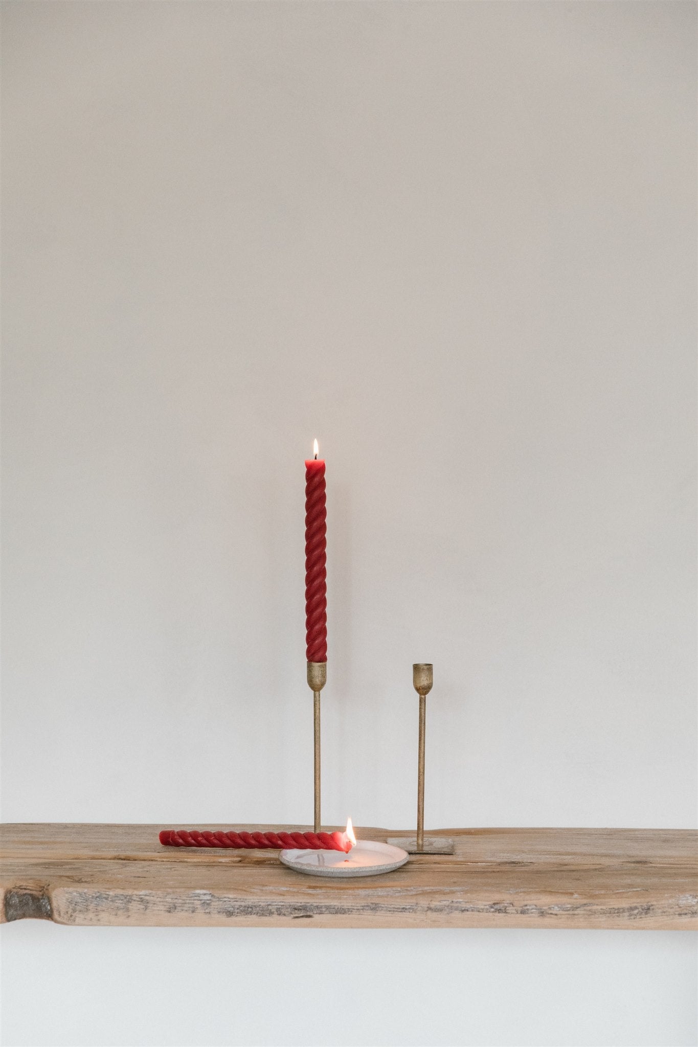 Red twisted beeswax taper candles in brass candlesticks on a rustic wooden table