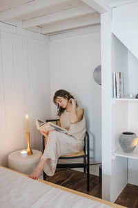 Woman sitting on a chair in a cozy nook reading a book next to a candles on a small table