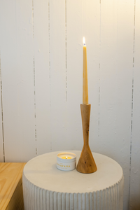 Natural beeswax taper candle burning in a wooden candlestick on a bedside table