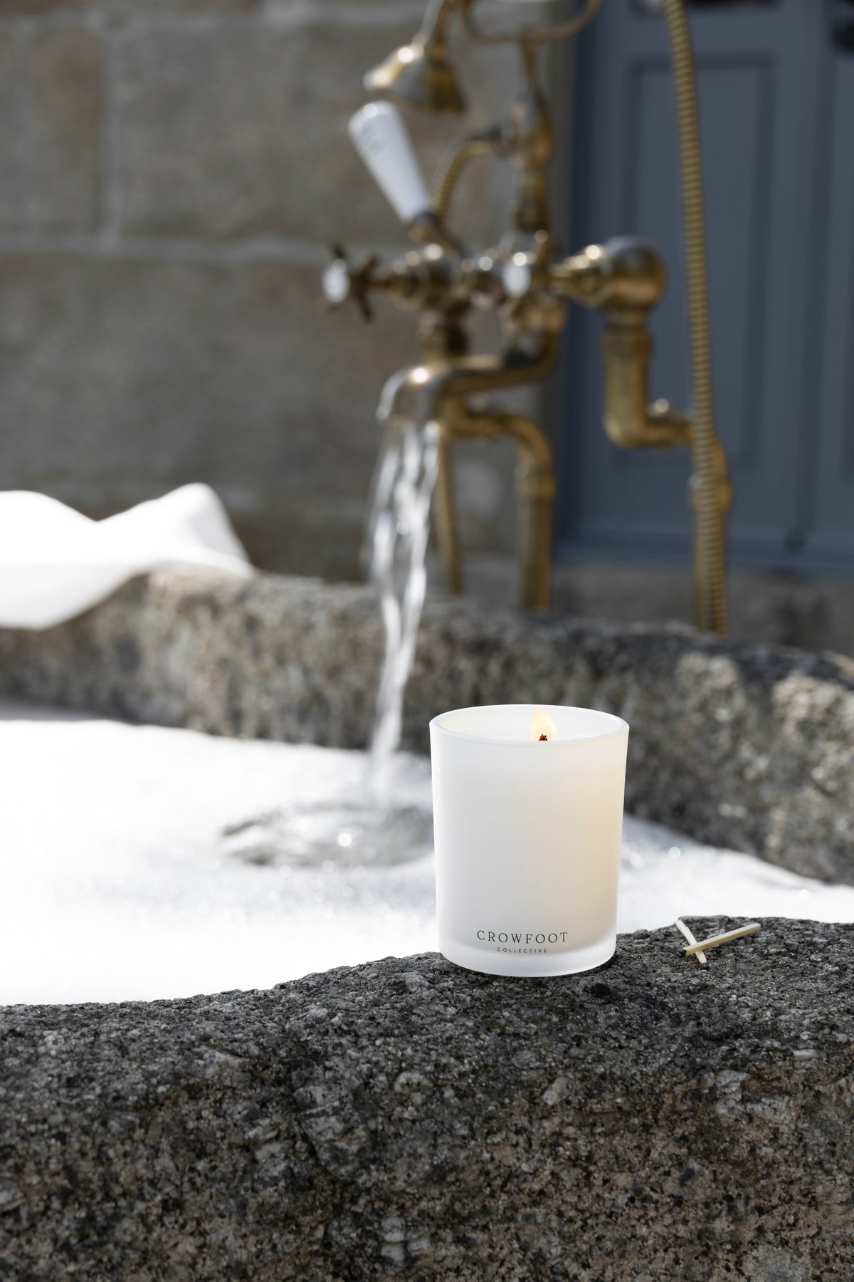 11:11 Classic candle in a white glass jar beside a stone bathtub with running water